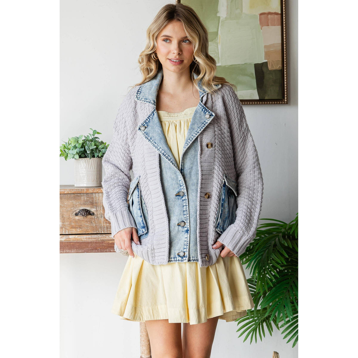 Woman wearing a light yellow dress and the Veveret - Knit Body Denim Layerd Jacket: Cream / Denim / L, standing indoors near a wooden table with a potted plant and framed artwork.