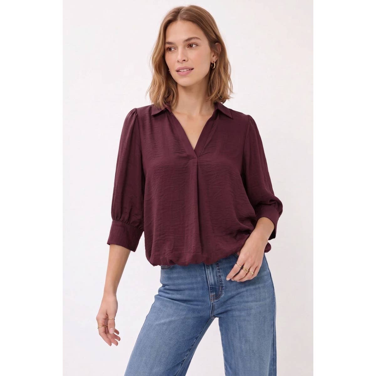 Woman wearing a Naked Zebra - Half Sleeve Hi-lo Bubble Hem Blouse: Wine / L, featuring a deep wine-colored bubble hem with half sleeves, a v-neck, and a collar, paired with blue jeans.
