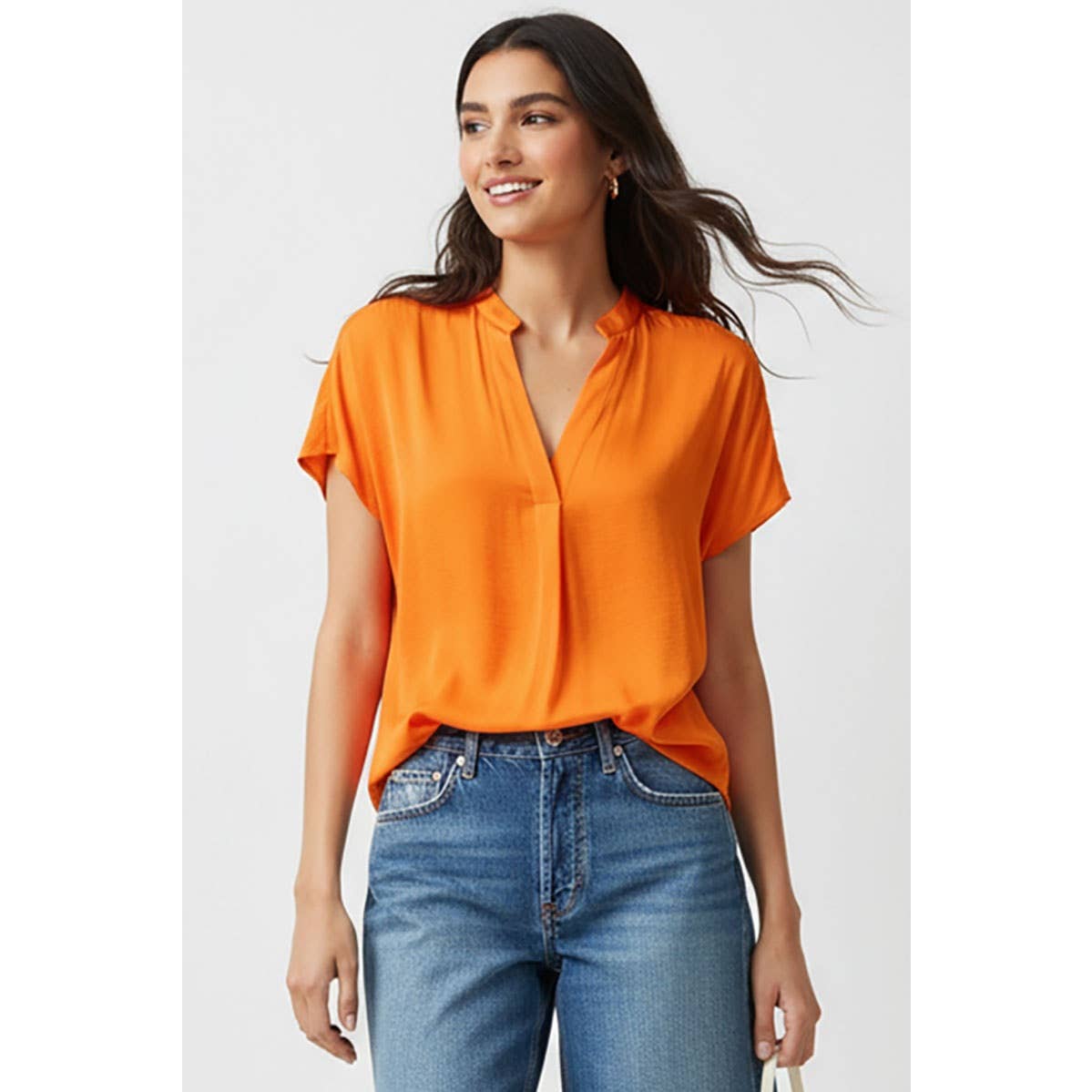 A woman wears a Naked Zebra - Drop Shoulder Regular Blouse in orange, featuring short sleeves, a drop-shoulder design, and a v-neckline, tucked into blue jeans.