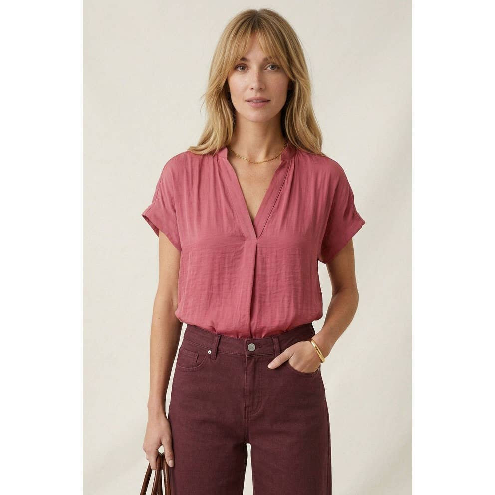 A woman wears a Naked Zebra - Drop Shoulder Regular Blouse: Chocolate / L with a V-neck and dark maroon pants.